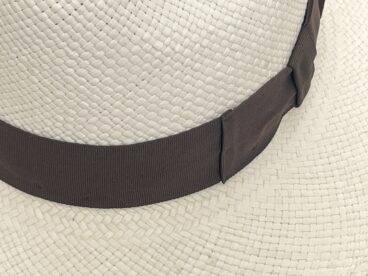 Nahaufnahme eines geflochtenen Strohhutes mit einem breiten Hutband in Dunkelbraun, das um die Krone gewickelt ist.