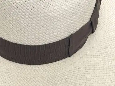 Nahaufnahme eines geflochtenen Strohhutes mit einem breiten Hutband in Dunkelbraun, das um die Krone gewickelt ist.